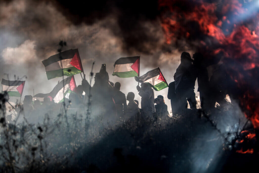 Silhouette of Palestnian protestors holding Palestinian flags with fire and smoke in the background, during a Palestinian 